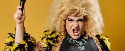 Libera la Tua Espressione 3 Una drag queen vestita in modo appariscente con una grande parrucca bionda, un'espressione accattivante e un microfono in mano